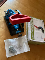 Fully assembled QuickMech angle grinder stand with red soft-grip handle next to original packaging and instruction manual on hardwood floor showing complete out-of-box experience
