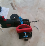 QuickMech adjustable stand showing dual-use capability with corded drill and drill bit clamped in place demonstrating versatility for both angle grinders and hammer drills